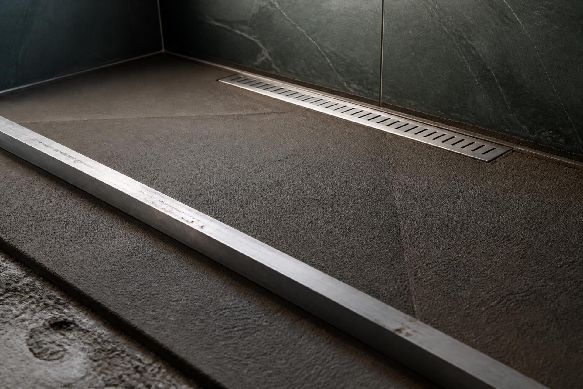 Freshly screeded shower floor mortar bed sloped toward a stainless linear drain