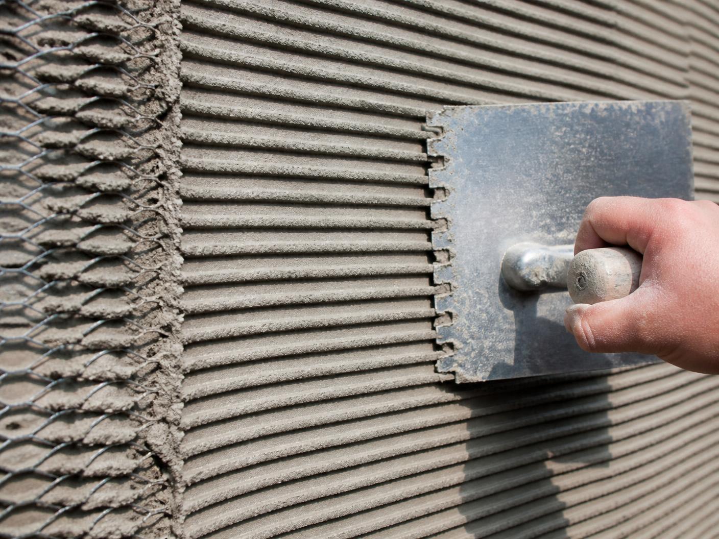 Notched trowel combing horizontal grooves into a cement scratch coat over metal lath
